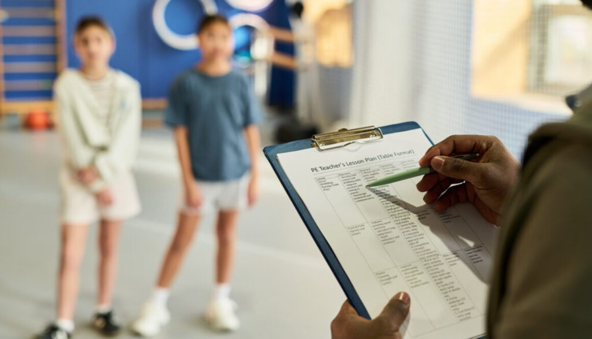 Male Coach Holding Clipboard Instructing Two Girls Indoors