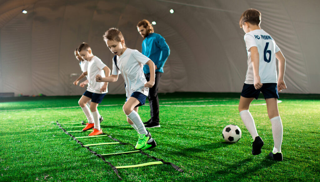 A busy soccer training facility with players practicing drills and coaches providing guidance, illustrating the essentials of running a well-organized program and offering insights into how to start a soccer training business.