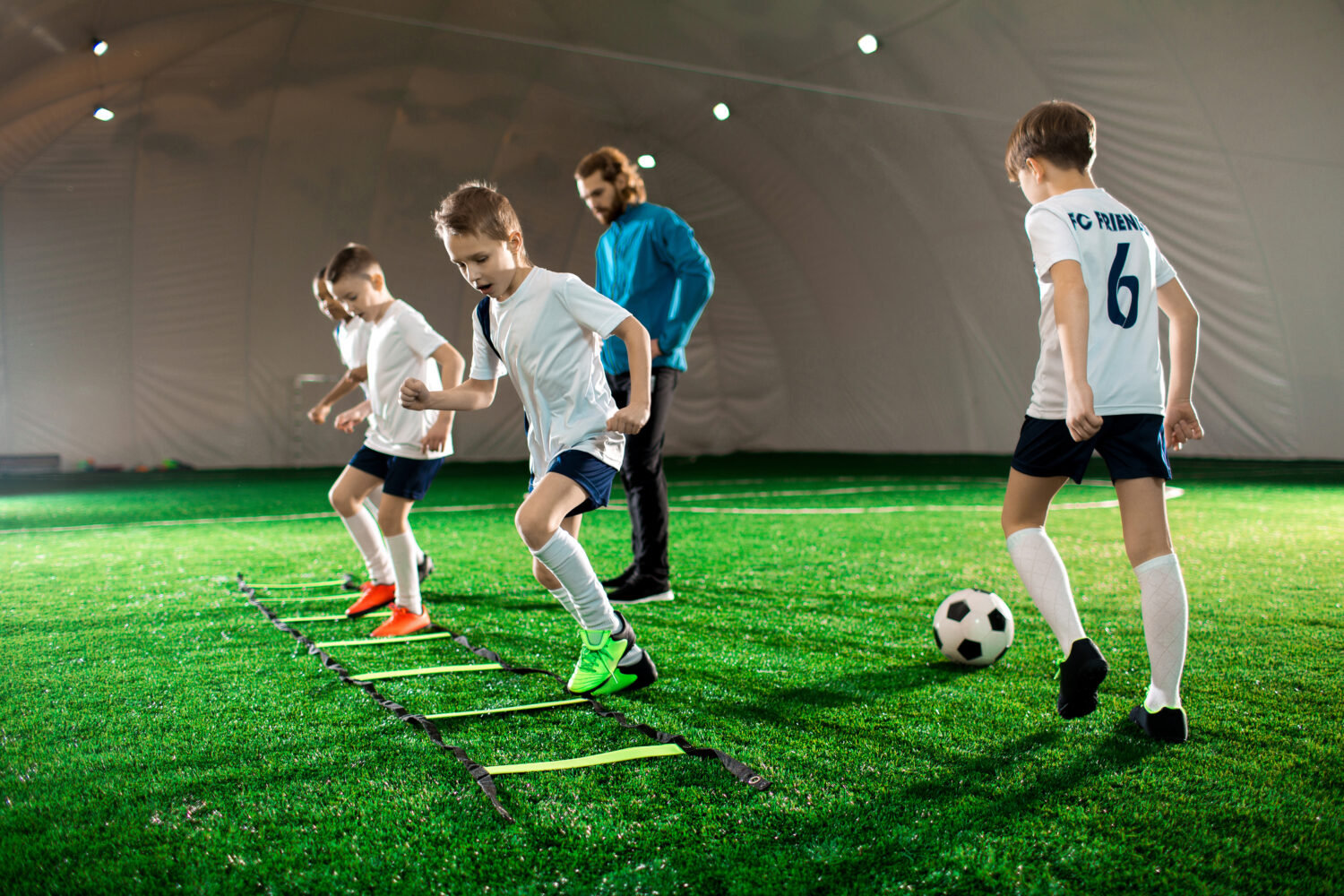 A busy soccer training facility with players practicing drills and coaches providing guidance, illustrating the essentials of running a well-organized program and offering insights into how to start a soccer training business.