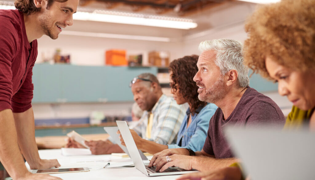 Teacher Helping Mature Man Attending IT Class In Community Centre