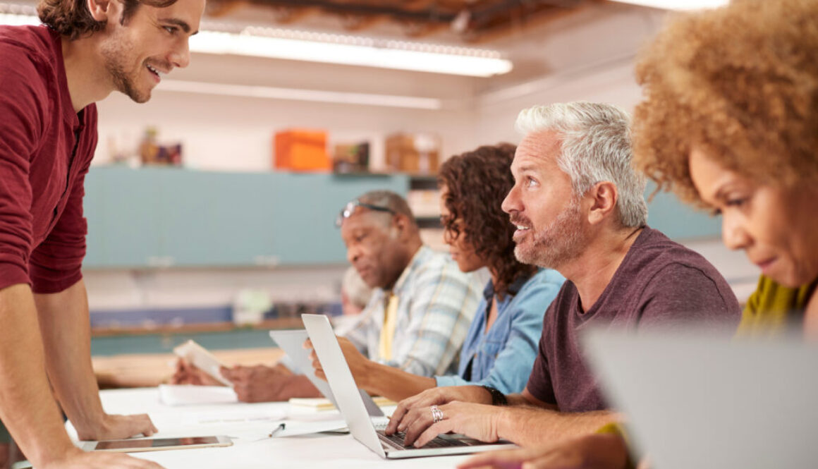 Teacher Helping Mature Man Attending IT Class In Community Centre