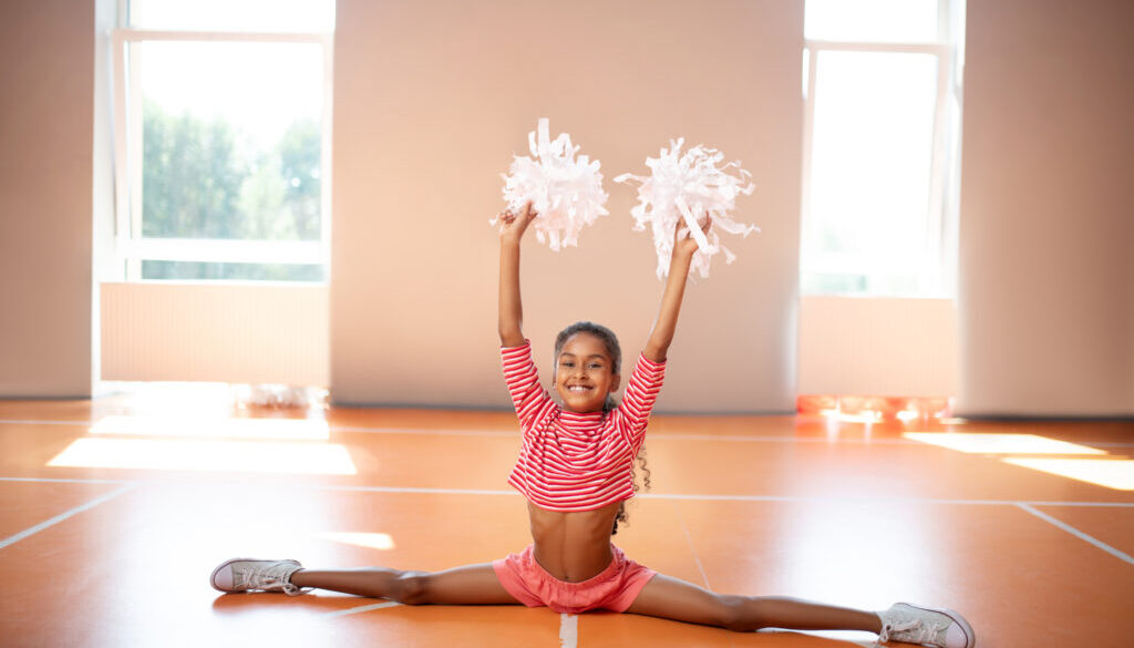 A young cheerleader practices a split with pom-poms in a cheer gym, a scene that highlights the possibilities of opening a cheer gym