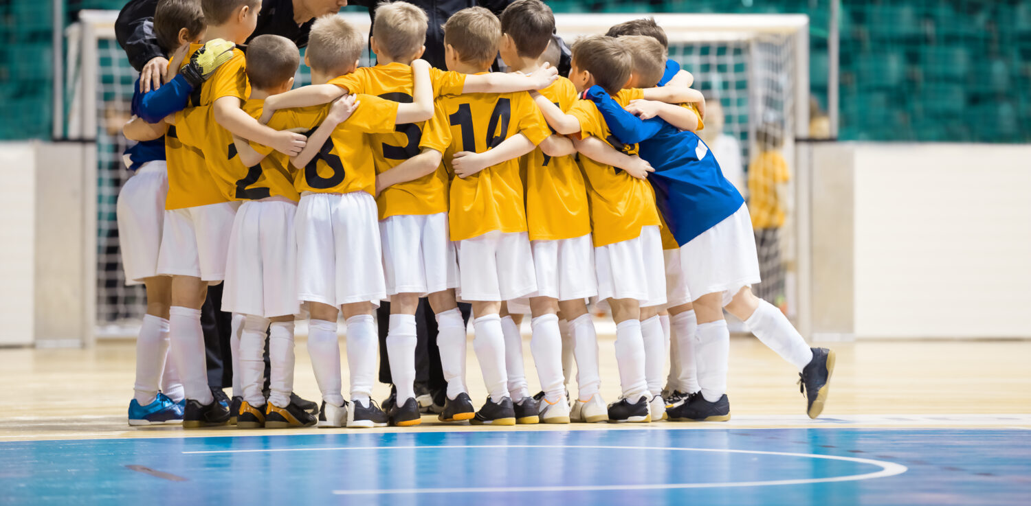 Young soccer players gather in a close huddle on an indoor court. It is an example of the team model from the different facility management models