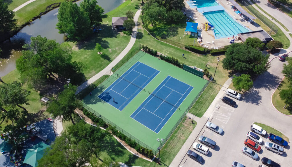 Aerial view of a pool and tennis club with two tennis courts, a swimming pool, and surrounding amenities, highlighting the need for efficient pool and tennis club software to manage reservations and memberships.