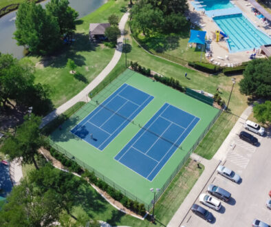 Aerial view of a pool and tennis club with two tennis courts, a swimming pool, and surrounding amenities, highlighting the need for efficient pool and tennis club software to manage reservations and memberships.