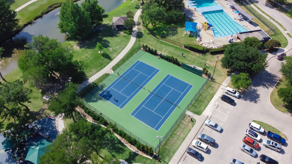 Aerial view of a pool and tennis club with two tennis courts, a swimming pool, and surrounding amenities, highlighting the need for efficient pool and tennis club software to manage reservations and memberships.
