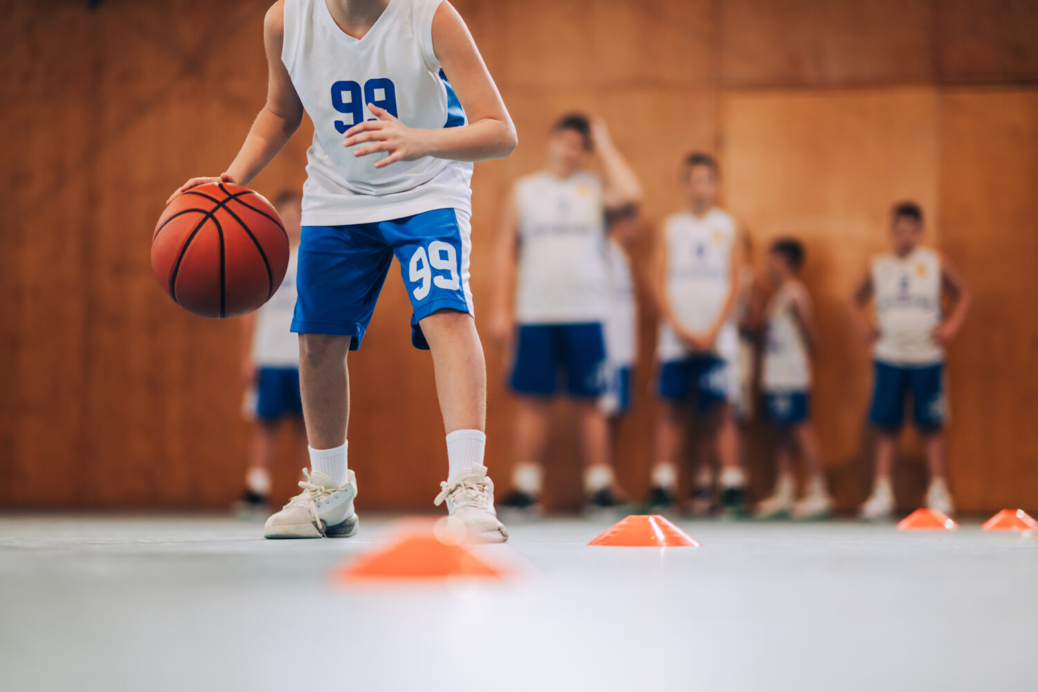 Cropped image of junior basketball player dribbling ball on training. Youth basketball player practicing ball handling drills during a training session, which is a common starting point for basketball training businesses.
